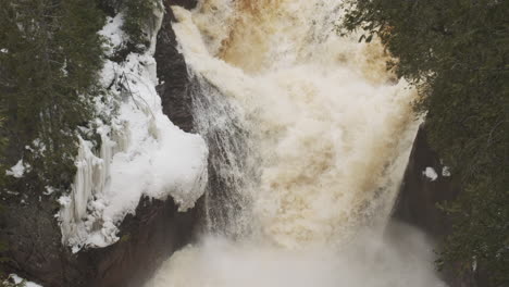 Eine-Kaskade-Eisigen-Wassers-Donnert-Einen-Winterwasserfall-Hinunter,-Angetrieben-Durch-Den-Fluss-Des-Schmelzenden-Schnees