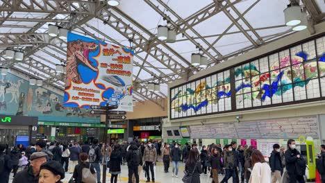 Bustling-Japanese-train-station-with-travelers-and-colorful-ads,-wide-shot