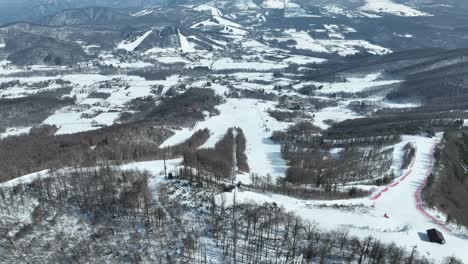 Establishing-push-in-pan-down-shot-from-above-mountain-peak-summit,-camera-revealing-large-ski-area