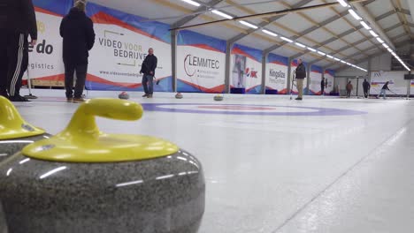 Yellow-granite-curling-stone-with-in-the-background-people-playing-curling-on-the-ice---Antwerp,-Belgium