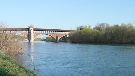 Bonita-Vista-De-Ponte-Coperto-Es-Un-Puente-Sobre-El-Río-Ticino-En-Pavia-En-Un-Día-Soleado,-Hombre-Navegando-En-Canoa,-Lombardia,-Pavia,-Italia