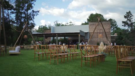 Sillas-De-Madera-Dispuestas-Para-La-Ceremonia-De-Boda-En-Un-Campo-De-Hierba-Frente-A-Un-Edificio-De-Eventos