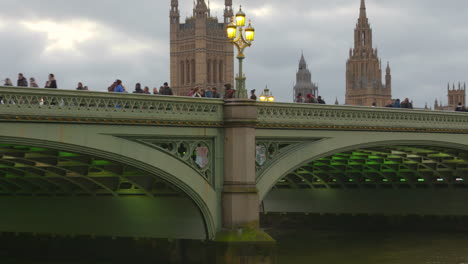 People-walking-on-Westminster-bridge-on-cloudy-day,-Palace-behind