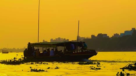 Passenger-boat-sailing-on-river-at-sunset-with-city-skyline-silhouette,-golden-hour