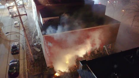 Firefighters-spraying-water-on-burning-building-in-Canadian-city-while-dark-toxic-fumes-rising-up---Aerial-tilt-down-shot