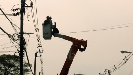 Un-Maestro-Electricista-Y-Un-Aprendiz-Están-En-Una-Grúa-Acercándose-A-Un-Poste-Eléctrico-Para-Hacer-Algunas-Reparaciones-En-Algunas-Conexiones-De-Cables