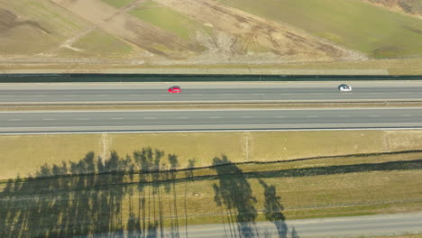 Luftaufnahme-Von-Spärlichem-Verkehr-Auf-Einer-Sonnenbeschienenen-Autobahn,-Gesäumt-Von-Grünen-Feldern