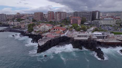 Camión-Aéreo-Izquierda-Toma-De-La-Costa-De-Catania,-Sicilia,-Italia-Con-Olas-Del-Mar-Rompiendo-En-El-Acantilado-Volcánico