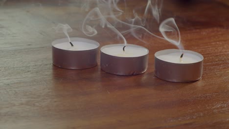 Three-tea-lights-on-table-smoke-when-blown-out,-closeup-view