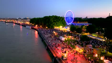 Riesenrad-In-Neonlichtern-Und-Menschenmassen-In-Bordeaux,-Frankreich-Bei-Sonnenuntergang,-Luftaufnahme-Eines-Überflugs