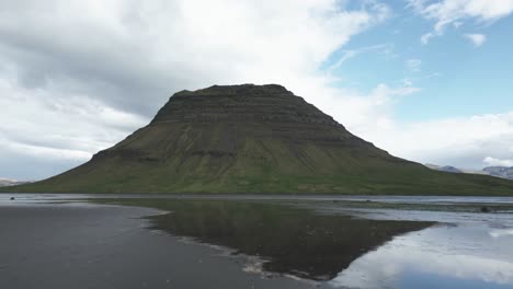 Low-flight-over-water-reflecting-lush-Kirkjufell-mountain-formation