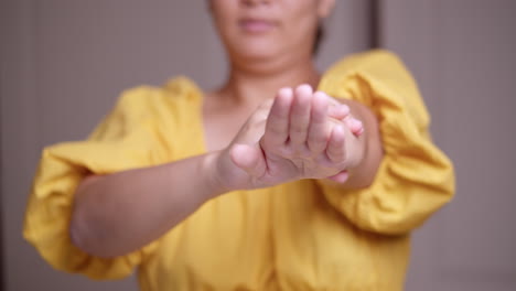 Woman-wearing-a-yellow-dress-is-stretching-out-her-left-arm-as-she-squeezes-and-massages-it-gently-down-to-her-fingertips