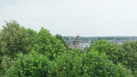 Revelar-Hacia-Atrás-Una-Toma-Aérea-De-Un-Dron-Del-Castillo-De-Laval-Detrás-De-Un-árbol-Verde,-En-Mayenne,-Francia