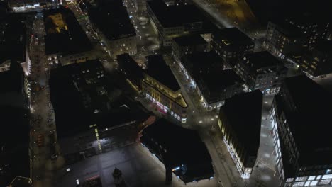 City-street-illuminated-by-urban-lights-and-buildings-in-Reykjavik,-aerial