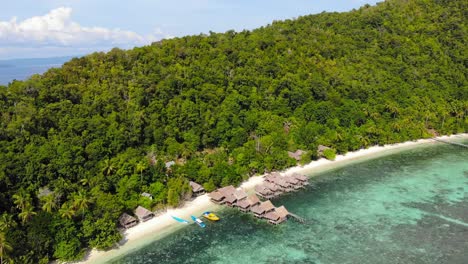 Resort-with-wooden-huts-and-thatched-roofs-along-exotic-beach-of-Kri-island-in-Raja-Ampat-archipelago,-West-Papua-in-Indonesia