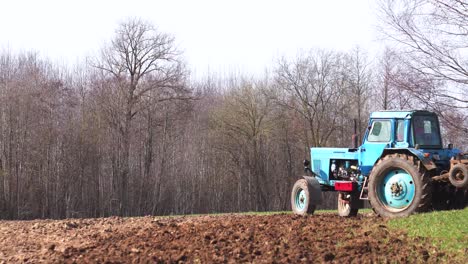 El-Granjero-Conduce-El-Viejo-Tractor-De-Producción-Soviética-Azul,-Cultiva-El-Campo-Agrícola