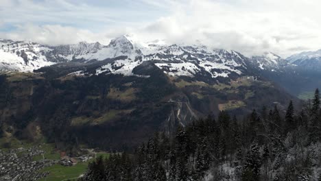 Desde-Un-Punto-De-Vista-Aéreo,-Se-Revela-El-Valle-De-Glarus,-Suiza,-Con-Comunidades-Residenciales-Enclavadas-En-Medio-De-Los-Majestuosos-Picos-Nevados-De-Los-Alpes-Suizos.