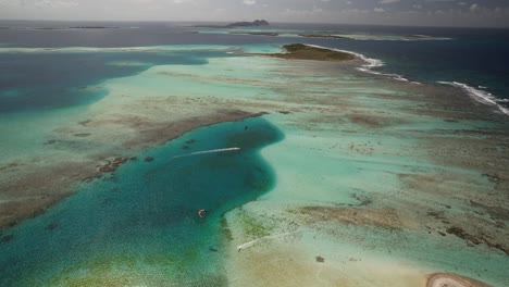 A-serene-tropical-cay-with-vibrant-turquoise-waters-and-coral-reefs,-under-a-clear-sky,-aerial-view