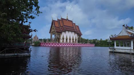 Traditional-Thai-temple-reflecting-in-water-at-Koh-Samui,-serene-sky-above,-surrounded-by-lush-greenery
