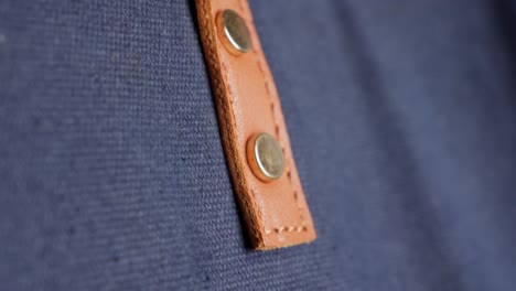 Close-up-of-a-tan-leather-belt-with-metal-rivets-on-blue-cotton-fabric,-detailing-textures