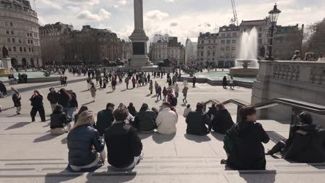 Gente-Sentada-En-Las-Escaleras-Con-Vistas-A-Trafalgar-Square-Con-La-Columna-De-Nelson-Y-Fuentes-Al-Fondo-En-Una-Mañana-Soleada