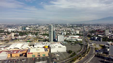 Aerial-approaching-shot-of-mexican-shopping-center-with-cityscape-of-Puebla-in-background