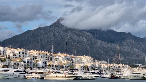 Closeup-of-a-Tall-Mountain-in-Puerto-Banus-Surrounded-by-White-Houses-and-Boats-Anchored-in-the-Harbour,-Spain