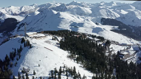 Un-Complejo-De-Montaña-Nevado-Con-Pistas-De-Esquí,-Remontes-Y-árboles-Alpinos,-Bajo-Un-Cielo-Azul-Claro,-Vista-Aérea