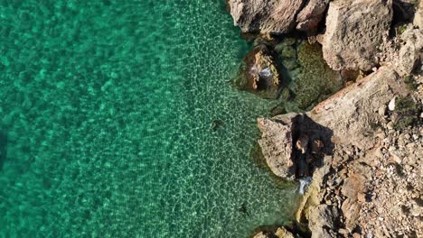 Mar-Cristalino-Y-Resplandeciente-Con-Playa-Rocosa-Tomada-De-Arriba-Hacia-Abajo-Con-Drones