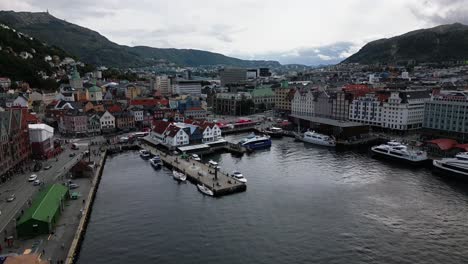 port-in-the-city-centre,-mounatins-with-forrest-in-the-background-of-the-city,-bergen,-norway,-europe,-drone