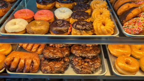 Primer-Plano-De-Una-Exhibición-Llena-De-Bocadillos-Dulces,-Donas-Y-Pasteles-Bajo-Las-Luces-De-La-Tienda.