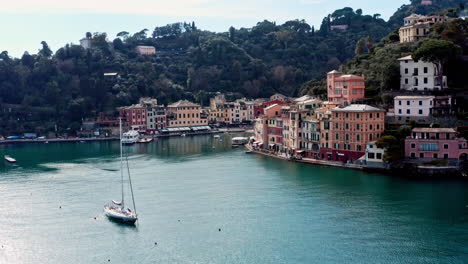 Sailboat-docked-on-Portofino-coastline-with-iconic-colorful-buildings,-aerial