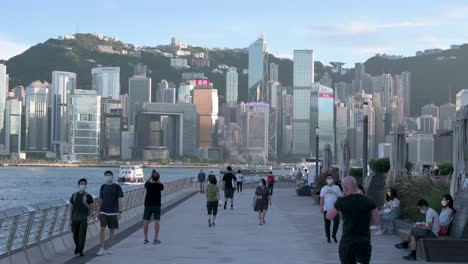 La-Gente-Camina-Por-El-Paseo-Marítimo-De-Victoria-Mientras-El-Horizonte-De-Hong-Kong-Se-Ve-Al-Fondo