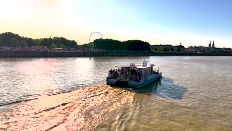 Gente-En-Barco-Recorriendo-El-Río-Garona-Con-Noria-En-El-Fondo,-Toma-Aérea-A-La-Derecha