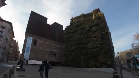 left-to-right-establishing-timelapse-shot-of-caixa-forum-museum-in-Madrid,-Spain-with-vertical-garden-facade-and-industrial-brick-on-a-sunny-winter-day
