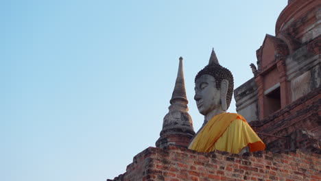 Große-Buddha-Statue-Mit-Orangefarbenem-Gewand-Im-Historischen-Park-Ayutthaya,-Thailand,-Gegen-Blauen-Himmel