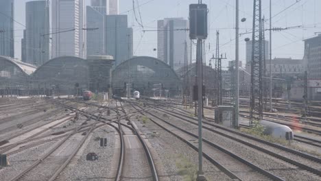 Busy-railway-station-with-multiple-tracks-converging,-city-skyline-in-the-background,-clear-day