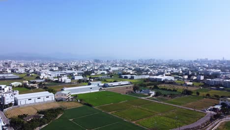 A-sprawling-suburban-landscape-with-fields-under-blue-skies,-aerial-view