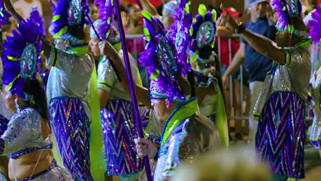 Old-man-holds-staff-wearing-silver-sparkling-costume-with-yellow-headdress-at-night-during-parade