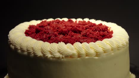 Primer-Plano-Detalle-Disparo-Pastel-De-Terciopelo-Rojo-Delicioso-Manjar-Sabroso-En-Una-Mesa-Giratoria-Fondo-Negro-Guarnición-Roja-En-La-Parte-Superior-Crema-Mantequilla-Afuera