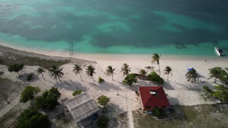 Stunning-Aerial-view-idyllic-tropical-island-with-palms-tree,-turquoise-sea-water,-Los-Roques-Venezuela