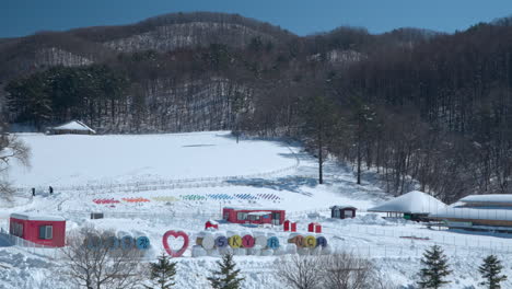 Aerial-view-of-Daegwallyeong-Sky-Ranch-in-winter-with-few-travelers-walking-by-farmlands-on-sunny-day