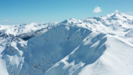 Snow-covered-mountain-peaks-under-a-clear-blue-sky,-aerial-view,-majestic-winter-landscape