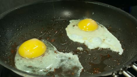 Two-raw-eggs-with-bright-yellow-yolks-fry-in-hot-oiled-pan-in-kitchen