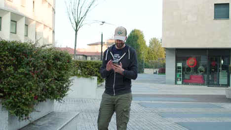 Un-Joven-Casual-Parado-En-El-área-Urbana-Desplazándose-Y-Tocando-El-Teléfono-Inteligente