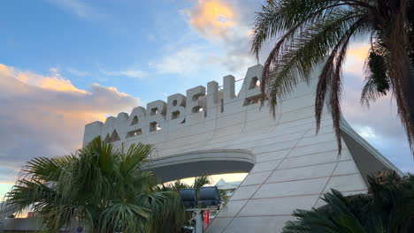 Big-Marbella-sign-with-sunset-orange-clouds-in-Spain,-pretty-sky-and-palm-trees,-4K-shot