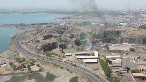 aerial-drone-drone-camera-view-showing-a-large-dumping-yard-near-a-large-river-and-many-cowsheds-and-residential-houses-around-where-vehicles-are-moving-on-the-road