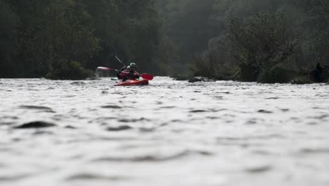 Rainy-River-Paddle,-3-Kayakers-Navigate-Through-the-Drizzle-in-slow-motion