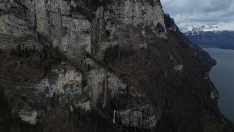 Drone-view-of-a-cliff-of-a-hill-with-mountains-at-background-in-Walensee,-Switzerland