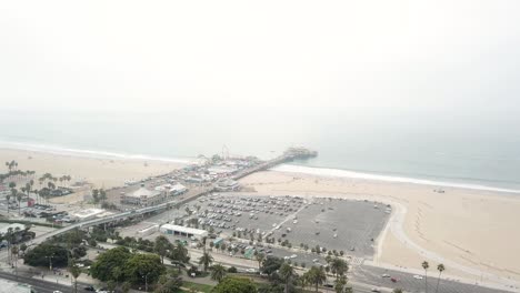 Vista-Aérea-De-4k-Del-Muelle-De-Santa-Mónica-En-Los-ángeles,-California,-Con-El-Océano-Con-La-Playa-Y-La-Ciudad-Al-Fondo